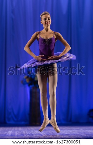 Young girl ballerina in a purple tutu dancing performance on stage in a theater on a blue and green background
