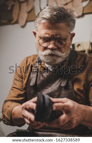 senior, bearded cobbler repairing shoe in workshop