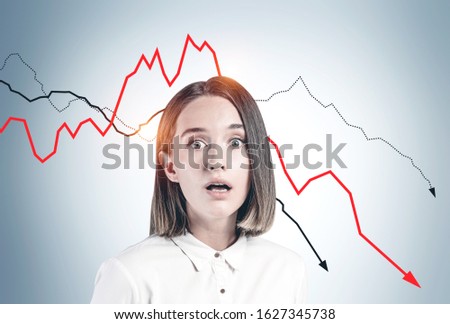 Desperate frightened young woman in formal clothes standing near gray wall with falling graphs. Concept of financial crisis and loss