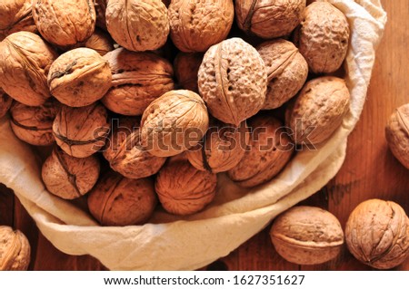Whole walnuts on rustic old wooden table, walnuts in a reusable cloth bag