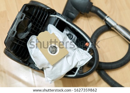 Dust bag full of dirt and the new empty dust bag lying near opened vacuum cleaner during a replacement of bags Royalty-Free Stock Photo #1627359862