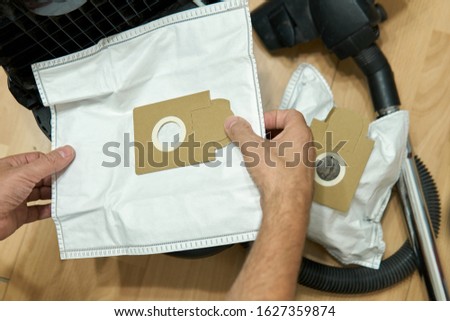 Man replacing dust bags in a vacuum cleaner at home during an apartment cleaning. Used dust bag full of a dirt lying near a vacuum cleaner Royalty-Free Stock Photo #1627359874