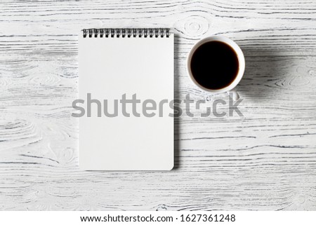 Notebook and cup of coffee on a white wooden table. Abstract background for design. Art stylized baner or mock up with copy space for a text.