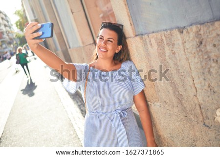Young beautiful woman smiling happy walking on city streets on a sunny day of summer taking a selfie photo using smartphone