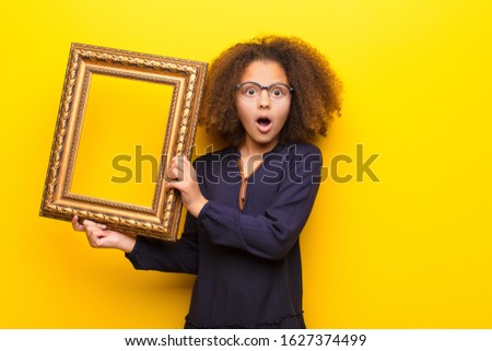 african american little girl  against flat wall holding a baroque frame