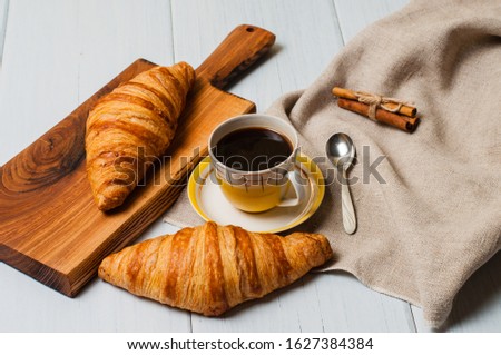 Coffee in a vintage yellow cup with a saucer, spoon and croissants with cinnamon on a wooden plate, linen napkin, on a light background, a rustic breakfast concept