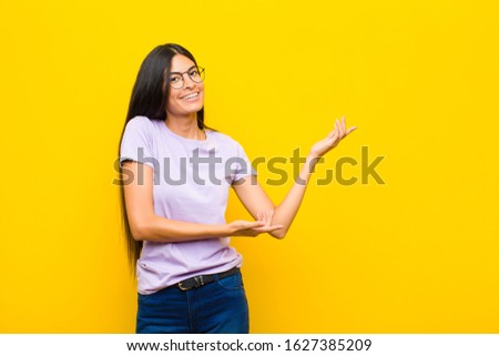 young pretty latin woman smiling proudly and confidently, feeling happy and satisfied and showing a concept on copy space against flat wall