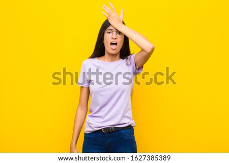 young pretty latin woman raising palm to forehead thinking oops, after making a stupid mistake or remembering, feeling dumb against flat wall