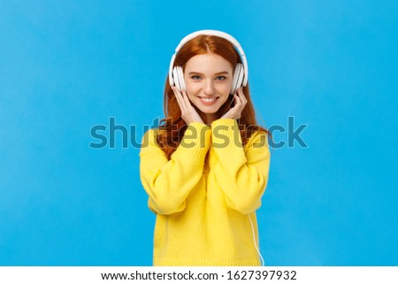Waist-up shot sassy good-looking redhead, ginger girl with blue eyes and freckles in soft yellow sweater, listen music headphones, press earphones to ears, smiling hear new song favorite singer