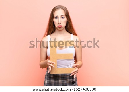 yound blonde woman sad, depressed, unhappy, holding the letter E of the alphabet to form a word or a sentence.