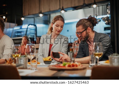 Cute caucasian fashionable couple sitting in restaurant at dinner and taking selfie.