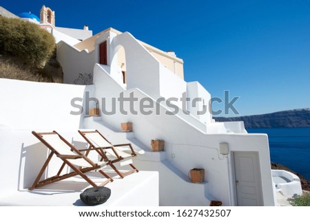 Pair of empty deck chairs sitting on the patio of a Greek island villa overlooking a scenic Mediterranean view of the caldera in Santorini, Greece