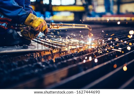 Worker cutting metal, steel with acetylene torch in big factory. Heavy industry, shipyard Royalty-Free Stock Photo #1627444690
