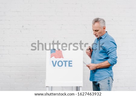 citizen holding pen while looking at ballot near voting stand