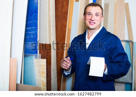 portrait of positive man in uniform choosing compressed densified wood in picture framing atelier