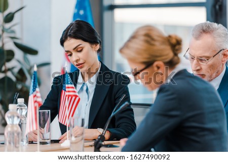 selective focus of attractive businesswoman near diplomats and flags of america