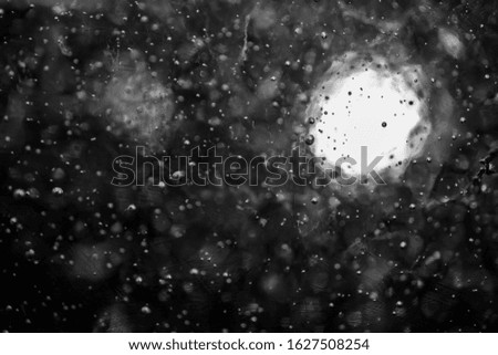 glass with raindrops and snow with glare, monochrome, blurred image