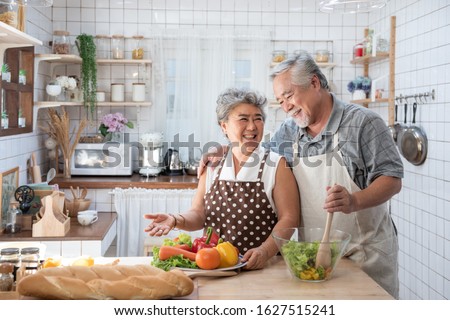 Senior couple having fun in kitchen with healthy food - Retired people cooking meal at home with man and woman preparing lunch with bio vegetables - Happy elderly concept with mature funny pensioner. Royalty-Free Stock Photo #1627515241