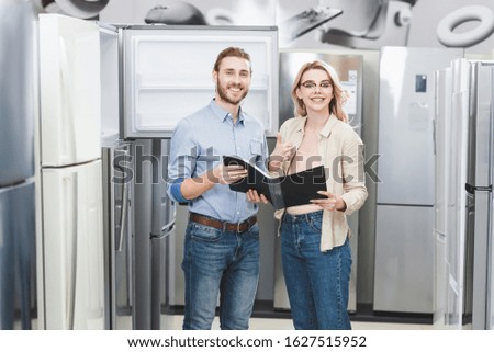 smiling consultant holding folder and woman showing like in home appliance store