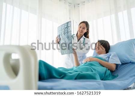 Doctor or physician take care of patient at the hospital.Beautiful female medical doctor is talking to patient reviewing brain X-ray picture,radiographic image,ct scan,mri, isolated hospital clinic.