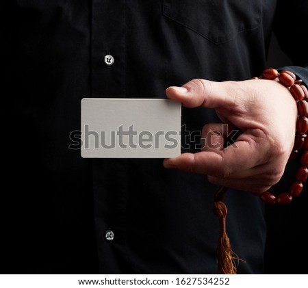 male hand holding a rectangular blank white paper business card, man wearing a black shirt, place for inscription