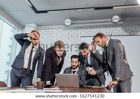 surprised caucasian business team cosisted of men in elegant suits, look at laptop surprisingly, stay in shock after results. isolated in modern office