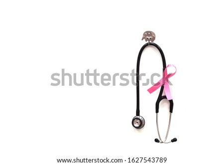   A black stethoscope hanging on the white wall with pink ribbon symbol of breast cancer prevention                             