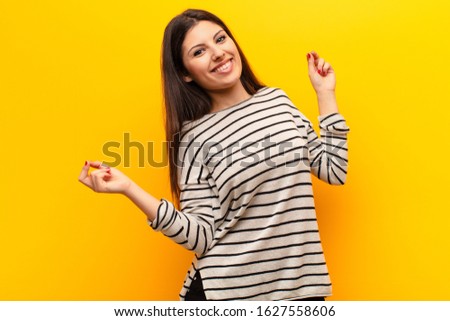 young pretty woman smiling, feeling carefree, relaxed and happy, dancing and listening to music, having fun at a party against yellow wall