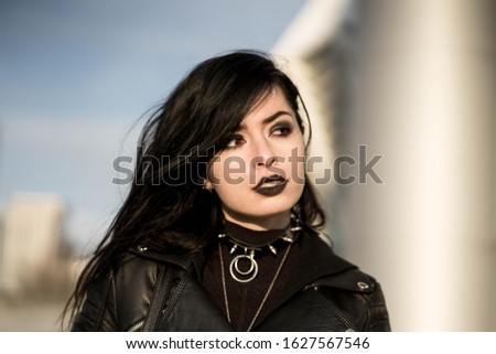 Portrait of a girl in black with black aggressive make up and massive jewelry in a city. Might be a picture representing subculture, youth, teenagers, evil, protest Royalty-Free Stock Photo #1627567546