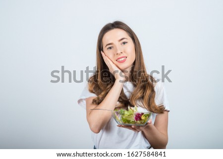girl in white t-shirt holds a bowl with salad in her hands and smiles on a white background. Healthy Eating