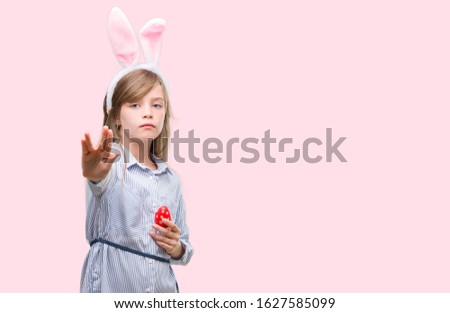 Young blonde child wearing easter bunny ears with open hand doing stop sign with serious and confident expression, defense gesture