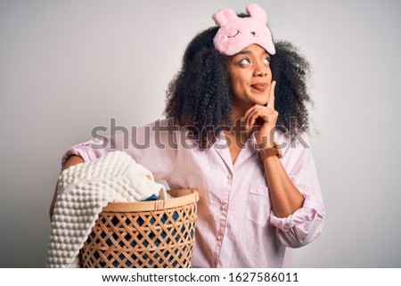 Young african american woman with afro hair wearing pajama doing laundry domestic chores serious face thinking about question, very confused idea