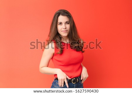 young pretty woman looking proud, confident, cool, cheeky and arrogant, smiling, feeling successful against red wall