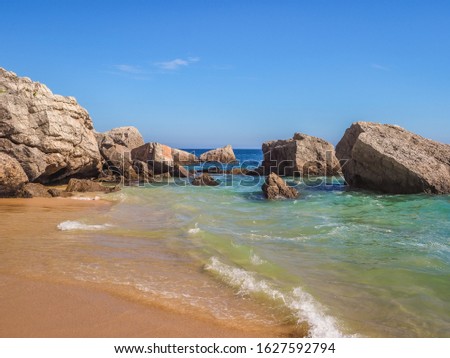 Beautiful landscape or seascape. Blue sea, sand and stones in coastline of Portugal. Surface waves scratch Atlantic Ocean shore with white water spray. Amazing sunny summer day. Photo wallpaper design