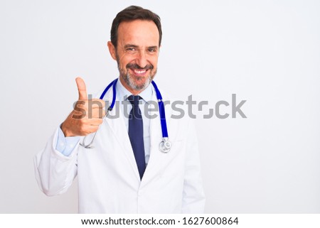 Middle age doctor man wearing coat and stethoscope standing over isolated white background doing happy thumbs up gesture with hand. Approving expression looking at the camera showing success.