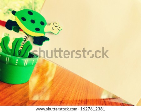 A green tortoise paper clip with a white blank paper on a shiny wooden table. White blank paper for text