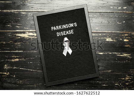 Board with text PARKINSON'S DISEASE and awareness ribbon on dark background Royalty-Free Stock Photo #1627622512