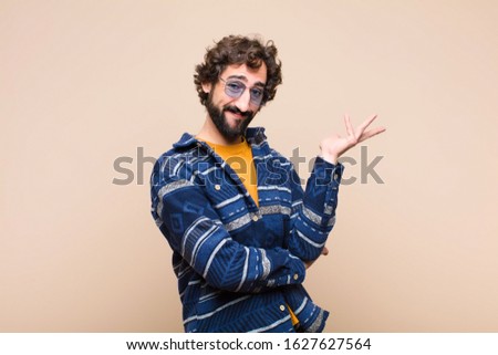 young crazy cool man smiling proudly and confidently, feeling happy and satisfied and showing a concept on copy space against flat wall