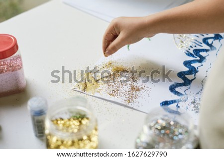 Child's hand using fingers for pouring sparkles for create a picture
