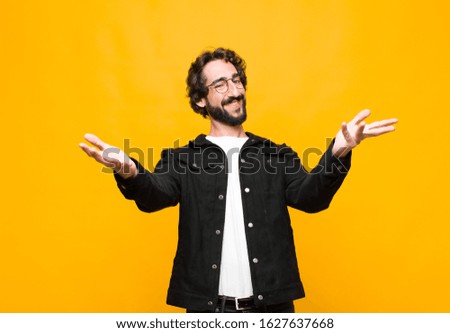 young crazy handsome man smiling cheerfully giving a warm, friendly, loving welcome hug, feeling happy and adorable against orange wall
