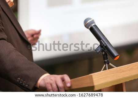 A man stands behind a stand with a microphone and holds a conference Royalty-Free Stock Photo #1627689478