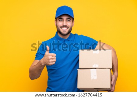 Delivery man over isolated yellow background with thumbs up because something good has happened