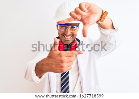 Young chemist man wearing security helmet and headphones over isolated background smiling making frame with hands and fingers with happy face. Creativity and photography concept.