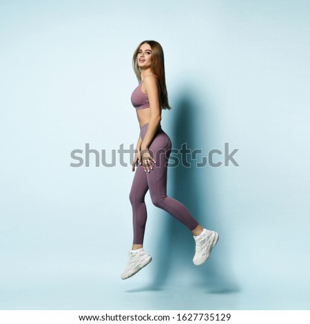 Sporty woman runner walking or running on light gray background. Attractive girl in modern fashionable sportswear make dynamic movement. Sport and healthy lifestyle concept