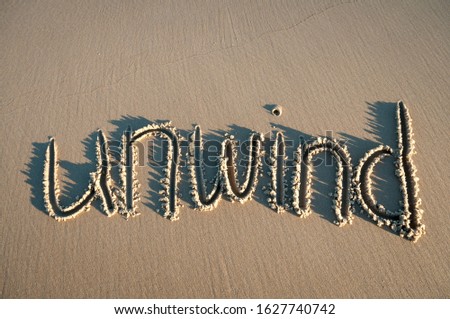 Unwind message handwritten in pristine brown sand with sun and shadows Royalty-Free Stock Photo #1627740742