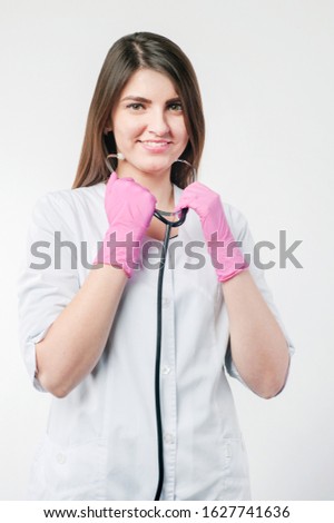 Portrait of smiling lady medical professional in white coat holding phonendoscope looking directly at the camera