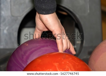 A hand holds a colored bowling ball. Wooden walkway in a bowling alley. Game with balls. Male hand takes the ball.