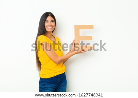 young latin pretty woman excited, happy, joyful, holding the letter E of the alphabet to form a word or a sentence.