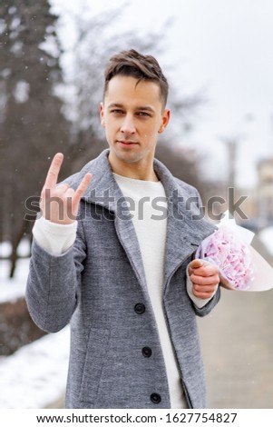 Boy friend with a bouquet of pink flowers hydrangea waiting for his girl friend outdoors while snow is falling. Valetnine`s day concept, wedding proposal. 
man goes on a date.