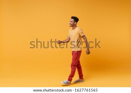 Side view of smiling cheerful young african american guy in casual clothes posing isolated on yellow orange background studio portrait. People sincere emotions lifestyle concept. Mock up copy space